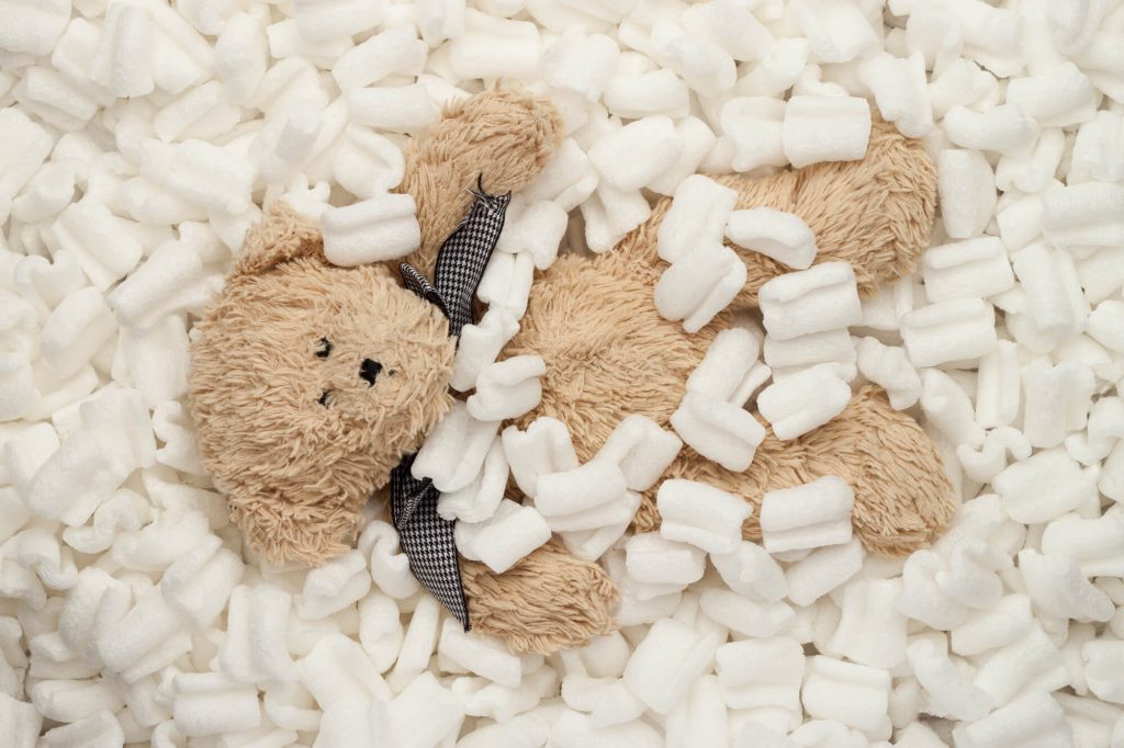 Teddy bear laying in a pile of 
 Styrofoam packaging in a box